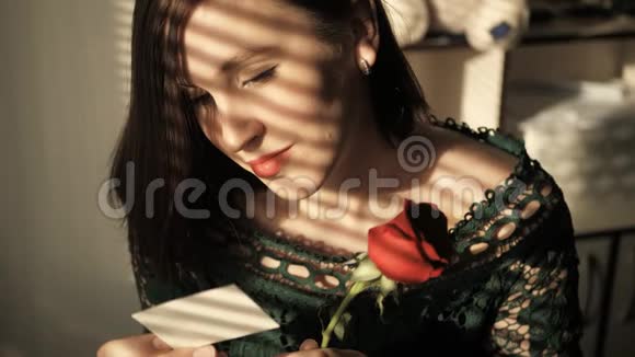 美丽的女孩坐在窗边的夕阳下读着纸条嗅着花看着窗外的爱情情人节视频的预览图
