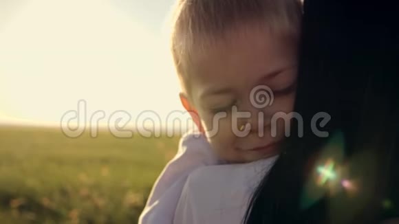 一个幸福的家庭年轻的母亲抱着她的小儿子在夕阳下的田野里笑家庭爱情概念视频的预览图