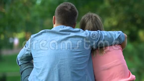 恋爱中的情侣坐在户外男人温柔地拥抱他的女孩背影视频的预览图