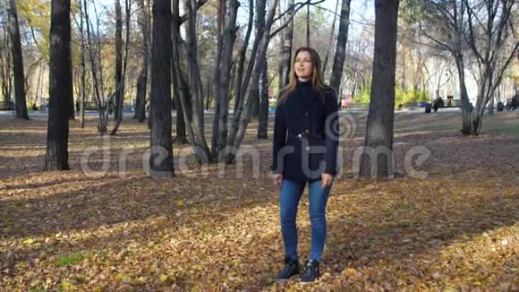 美丽的女人在秋天公园的落叶中缓慢地旋转4k60fps穿着外套的女孩走在视频的预览图