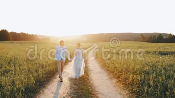 新郎新娘牵着手相视着爱情走着乡间的路夕阳红视频的预览图