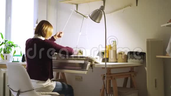 坐在车间桌子上的织布机上编织纺织品的年轻妇女视频的预览图