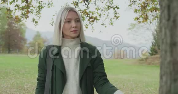 白人金发女人斯洛莫走向秋天的树林触摸树在前面的万向节后面讲故事真年轻视频的预览图