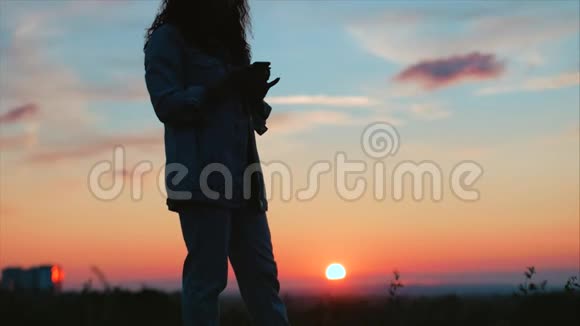 美丽的女人用双手在夕阳下做心形女孩用橙色的太阳耀斑举起爱情象征的手势视频的预览图