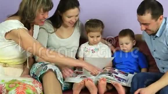 有孩子的父母和祖母考虑一张带有照片的相册幸福的家庭在等第三个孩子视频的预览图