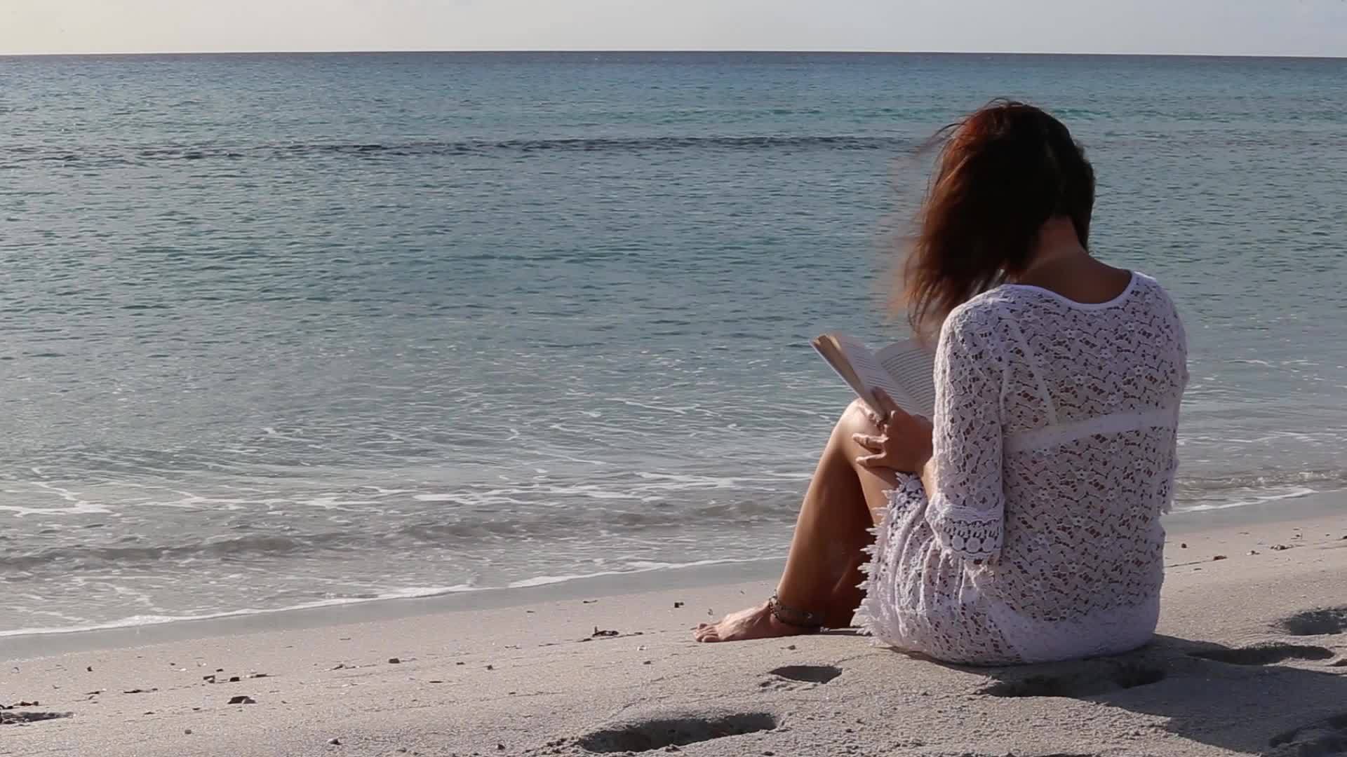 坐在海边的年轻女孩看着黎明风中的地平线穿着衣服视频的预览图
