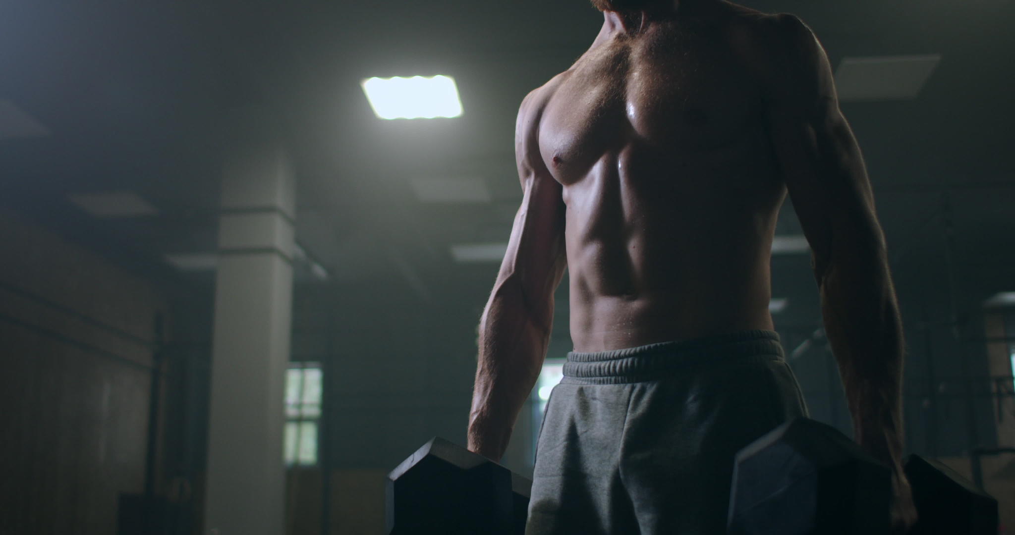 一个手里拿着哑铃的强壮男人在健身房弯腰视频的预览图