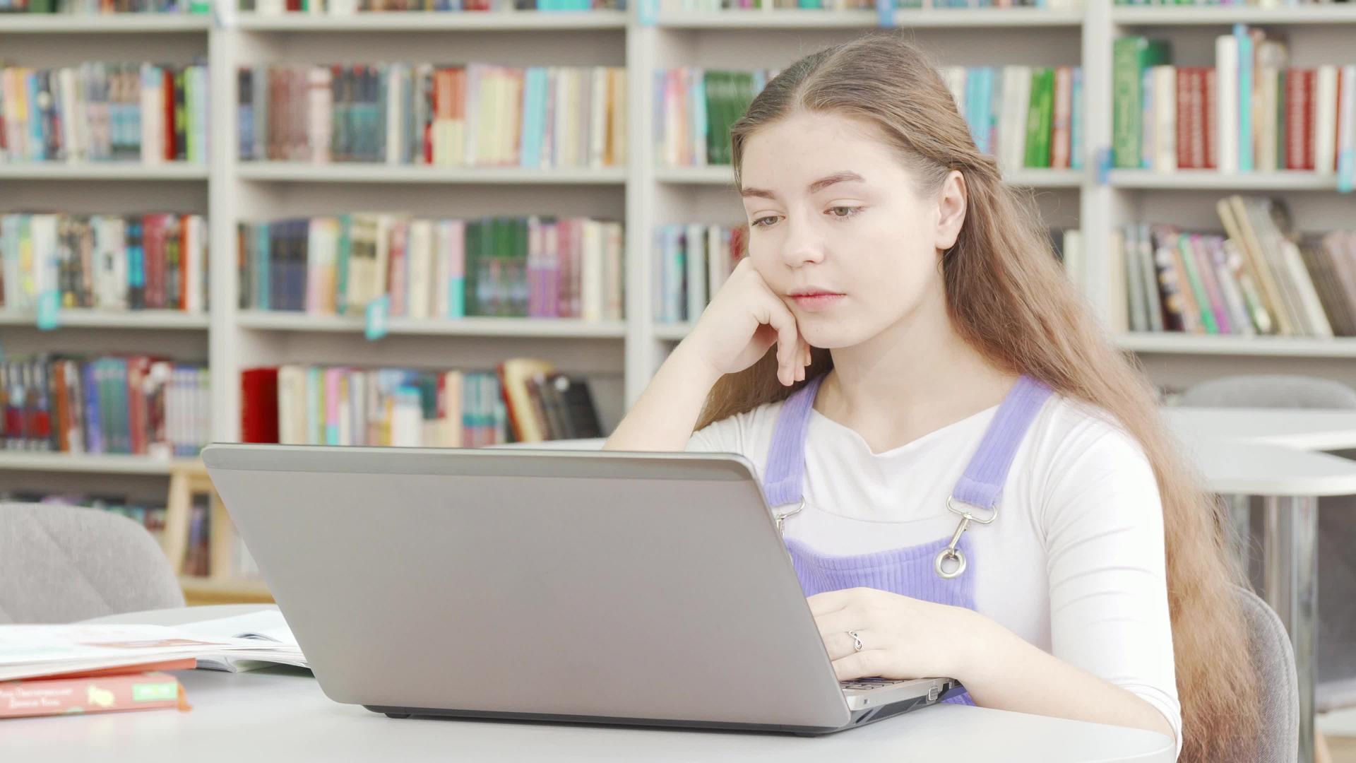 疲惫的女孩在图书馆的笔记本电脑上工作视频的预览图