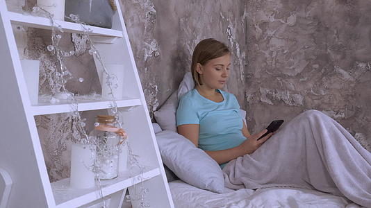 在卧室里使用智能手机的美丽caucasian女人视频的预览图