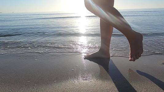 一个年轻女子的腿在岸边行走海浪拍打着她的脚在黎明时分视频的预览图