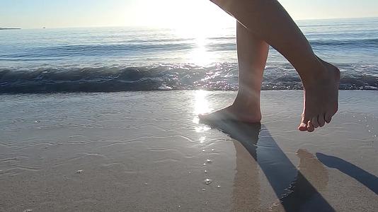 一个年轻的女人沿着海岸慢慢地走着海浪拍打着她的脚视频的预览图