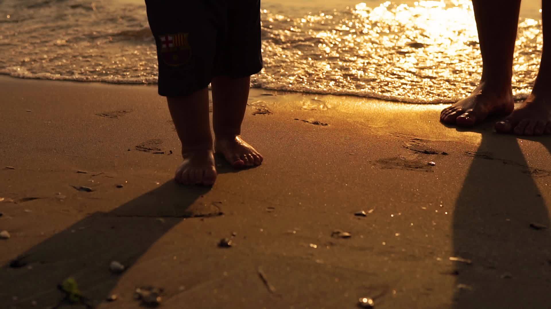 日落时 婴儿和孩子们在海边的沙滩上走来走去 慢慢地关上脚视频的预览图