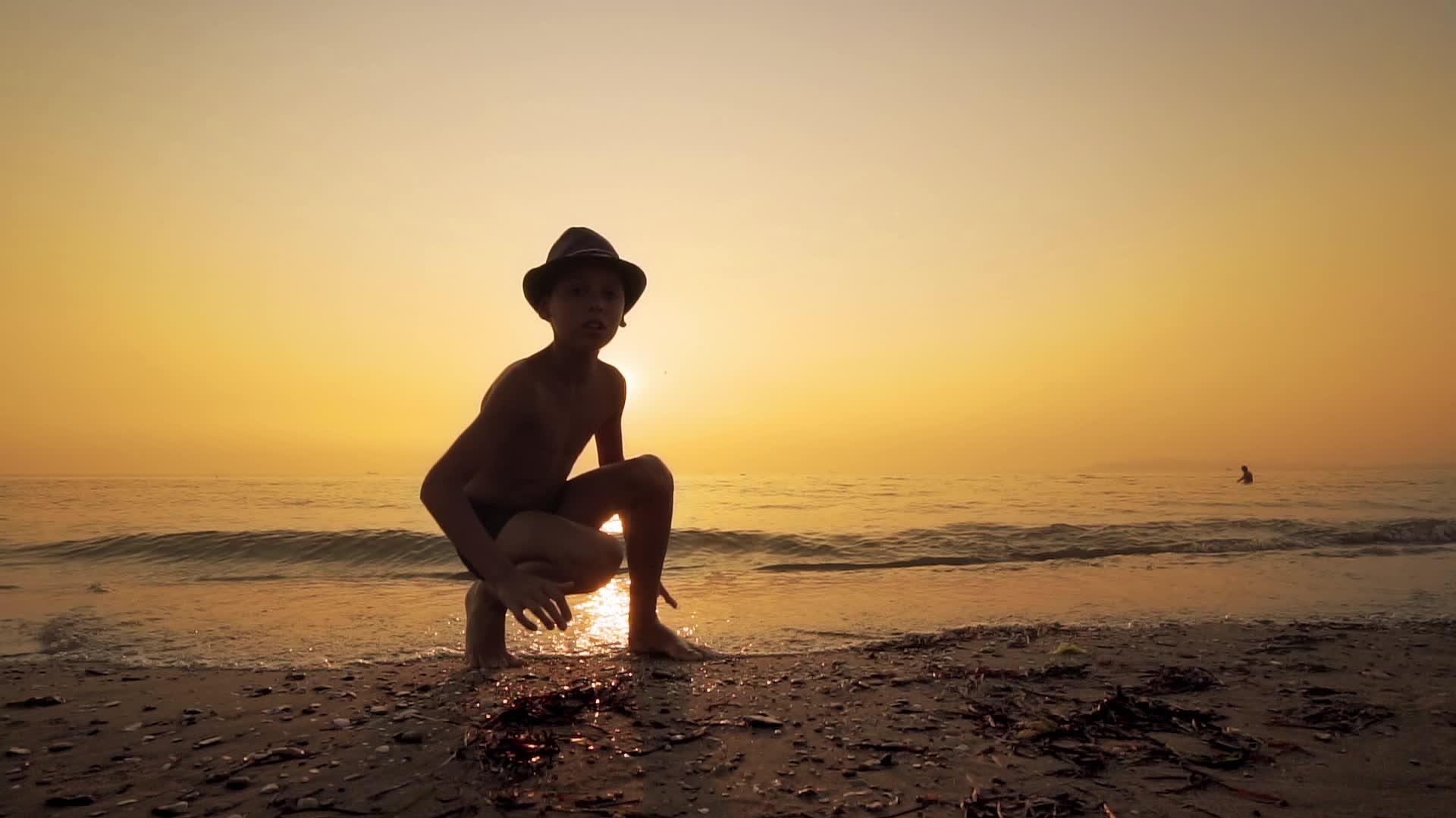 日落时小男孩在海边收集石头慢慢地移动视频的预览图