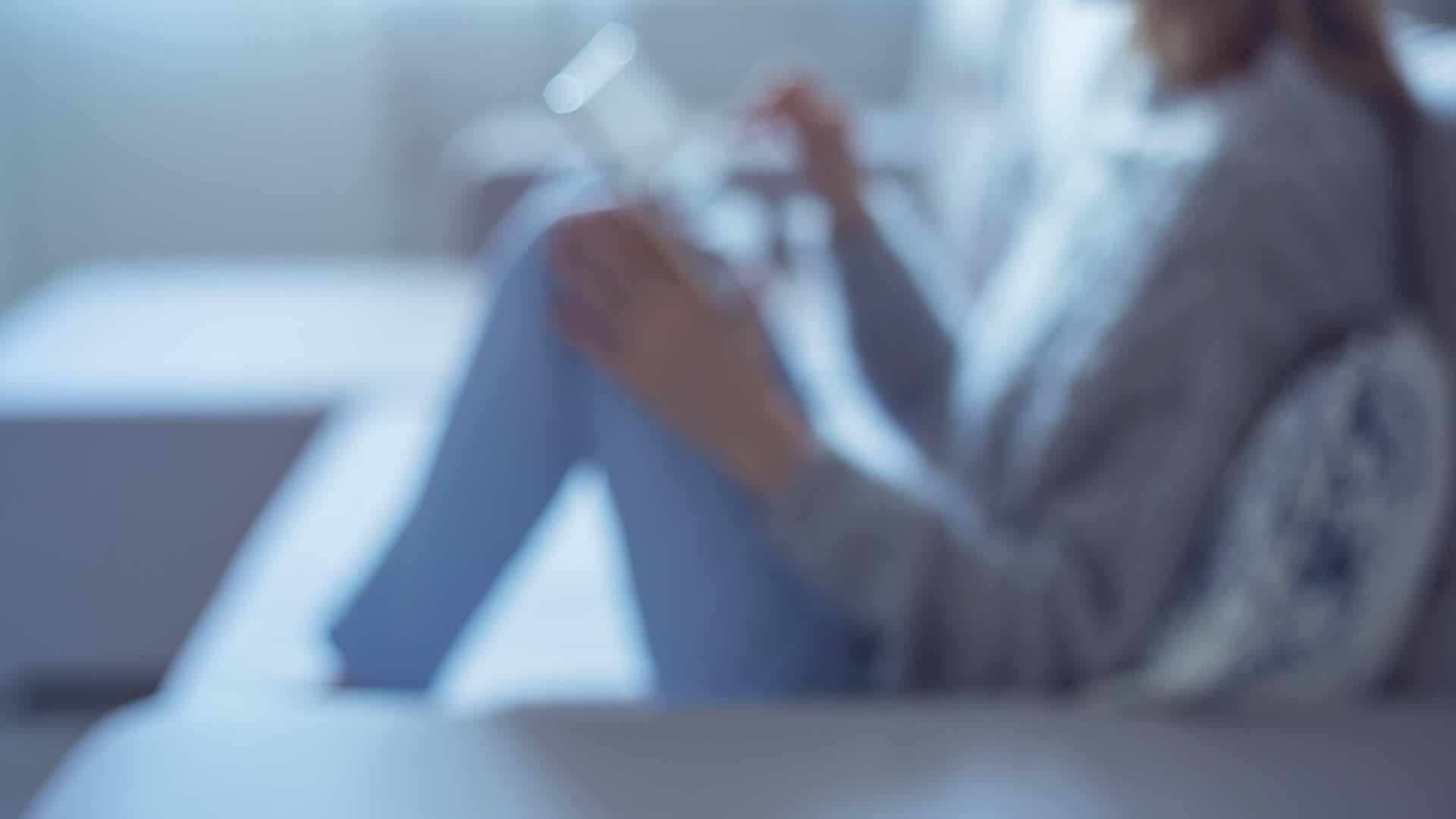 穿着蓝色牛仔裤的漂亮女孩用平板电脑坐在家里的灰色沙发上视频的预览图