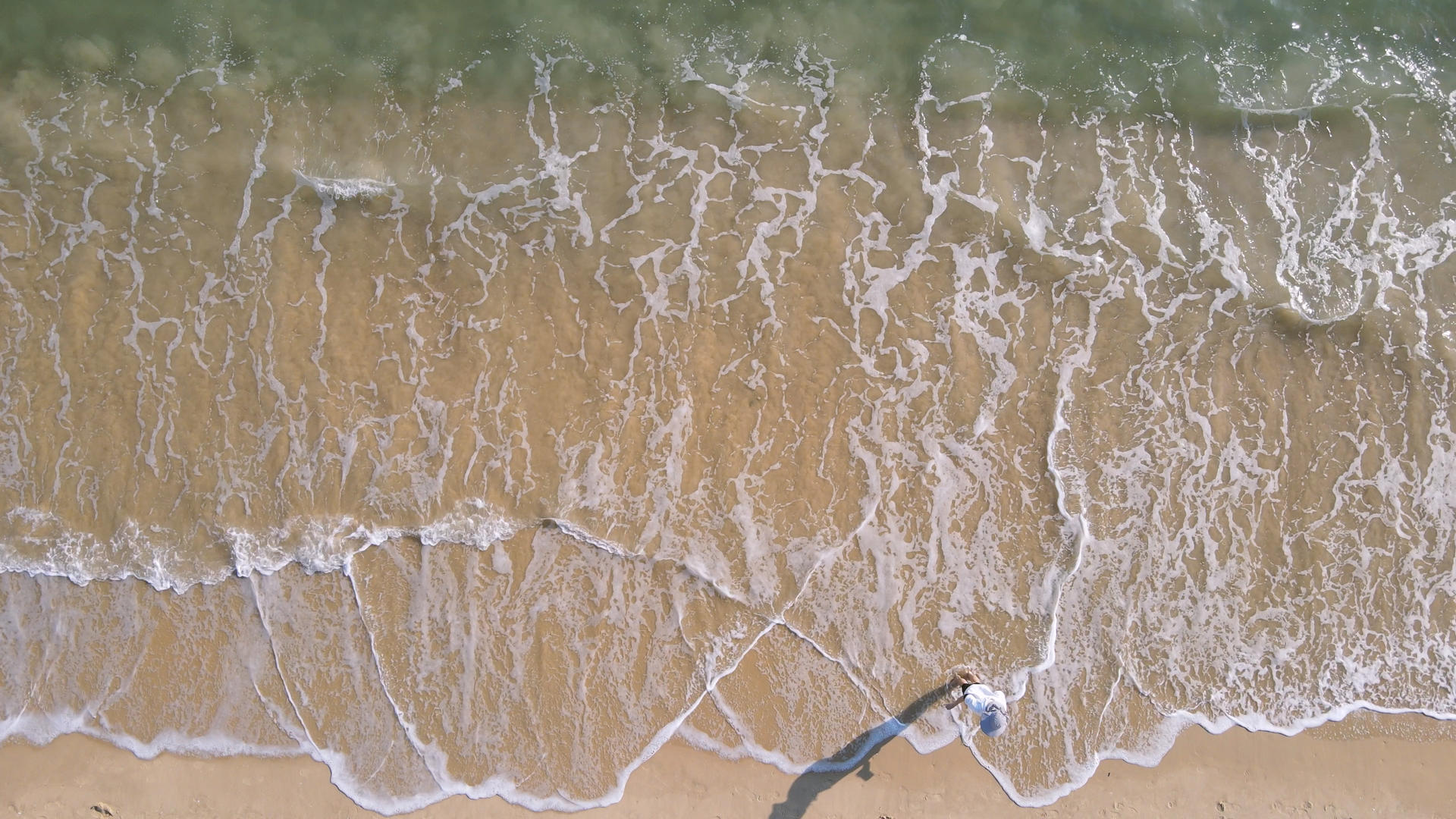 航拍海边沙滩上与海浪玩耍的少女4k素材视频的预览图