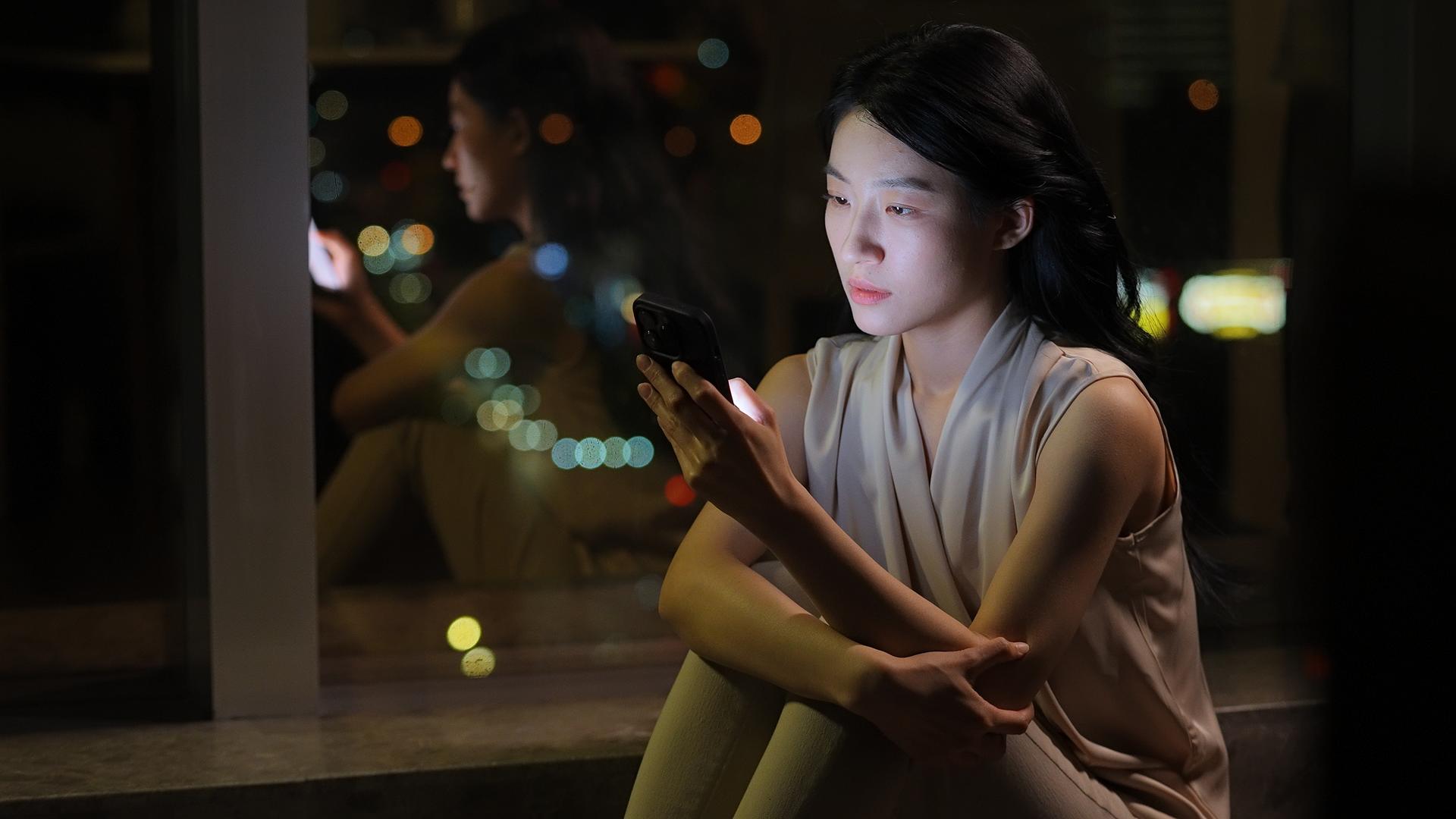 女人晚上窗边看手机情绪低落视频的预览图