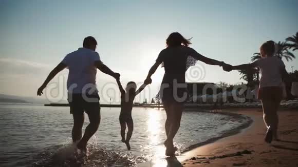 快乐的年轻家庭在日落时在海滩上散步很有趣家庭剪影旅游度假视频的预览图