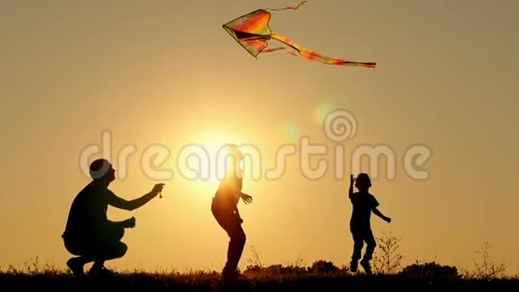 日落时分幸福家庭的剪影父亲和两个儿子在阳光明媚的背景下放风筝休息和玩耍视频的预览图