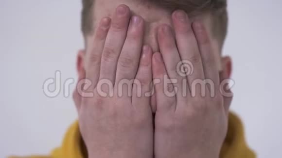 特写一个害羞的年轻人从后面的手指看着相机用手捂住脸隐藏的概念视频的预览图