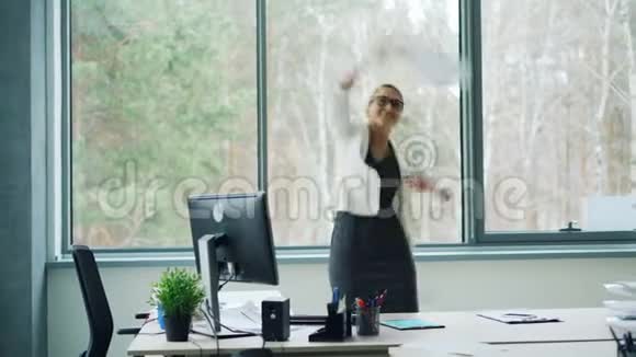 令人愉快的女商人在工作中放松高兴地听到好消息喊叫扔办公室文件跳舞和视频的预览图