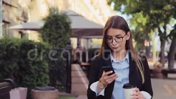 年轻的商务女性走在街上在午休时喝咖啡和使用智能手机视频的预览图