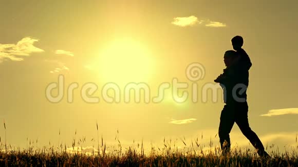 父子在夕阳背景下散步的剪影爸爸把他的儿子抱在肩上a的概念视频的预览图