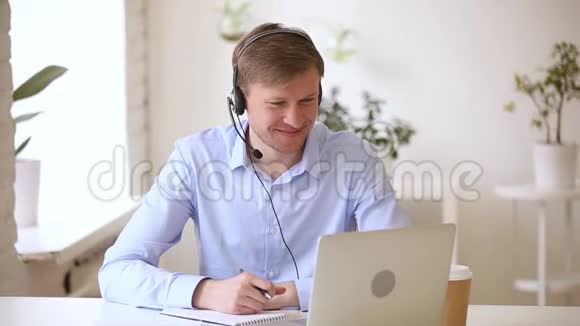 微笑商人戴着耳机在网上学习做笔记视频的预览图