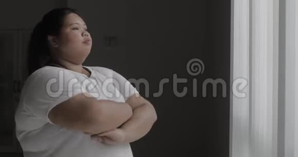 沮丧的超重女人站在窗户附近视频的预览图