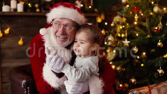 小女孩低声说圣诞老人听她的圣诞愿望坐在他的腿上视频的预览图