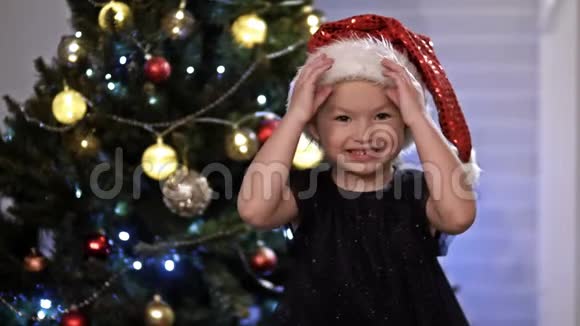 戴圣诞帽的小女孩在圣诞树附近玩捉迷藏玩的心情视频的预览图