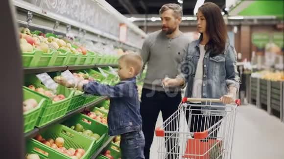 有孩子的年轻家庭正在超市买食物父母正在挑选水果男孩正在把它们放进超市视频的预览图