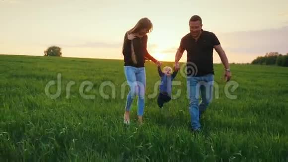 一对幸福的父母和一个小儿子正穿过田野走向日落有孩子的幸福家庭视频的预览图