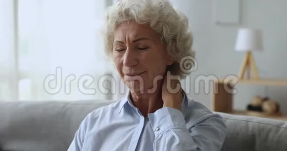 不高兴疲惫的老年妇女在家摩擦颈部感到疼痛视频的预览图