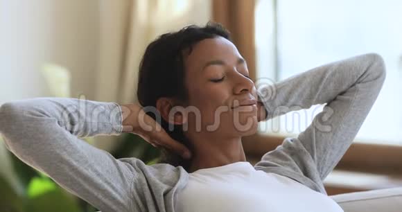 放松的非洲女人躺在舒适的沙发上在家里做梦视频的预览图
