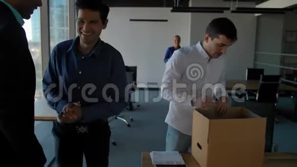 年轻员工用文档和设备打开包装盒他的同事走在现代办公室附近视频的预览图