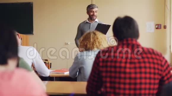 高中老师帅哥正在和坐在教室里的桌子旁微笑的学生交谈教育视频的预览图
