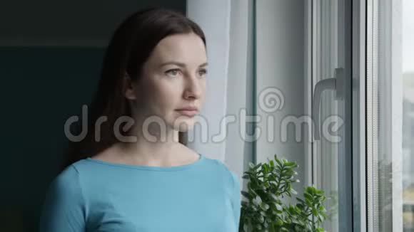 可怜的中性脸表情站在窗前看镜头拍摄的可怜女人的画像视频的预览图