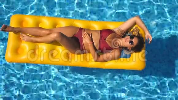 在游泳池里的黄色充气床垫上可以看到美丽的晒黑女孩戴着太阳镜和红色比基尼视频的预览图