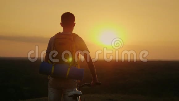 一个带背包和自行车的人它站着看着太阳落下的地平线骑自行车和冒险视频的预览图