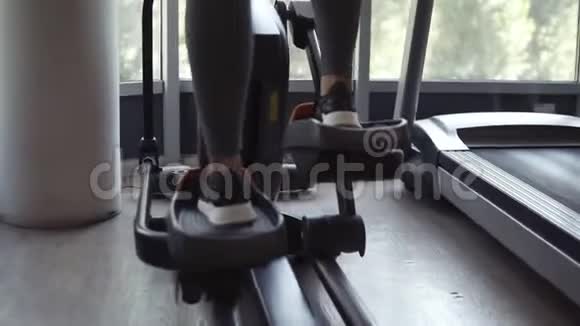健身中心的椭圆训练器的目标镜头健身房里靠近窗户的健身女孩生活方式视频的预览图