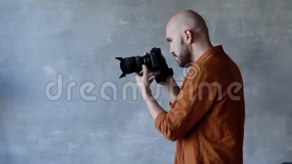 年轻英俊的摄影师留着胡子在摄影棚里用专业的相机拍照后台后台视频的预览图