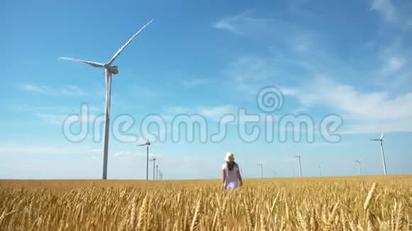 美丽的女孩走在黄色的麦田上用风车发电视频的预览图