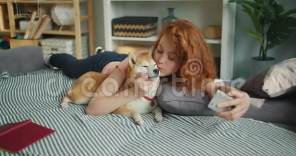 十几岁的女孩在家里用智能手机摄像头与狗吻宠物自拍视频的预览图