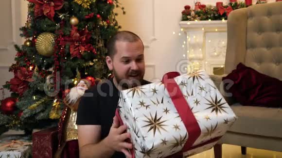 坐在圣诞树旁的一个长胡子的漂亮男人送了一份礼物视频的预览图