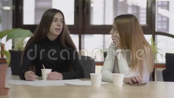 两位同事在休息时坐在现代商务办公室的桌子旁聊天喝咖啡概念视频的预览图