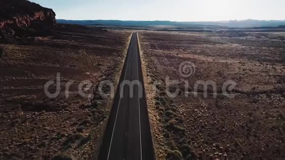 无人机在美国荒野的笔直沙漠公路上向前飞行靠近巨大的岩石山和美丽的天空视频的预览图