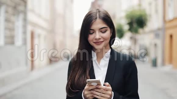 年轻漂亮的商业女性使用智能手机走在老街上她上网概念新视频的预览图