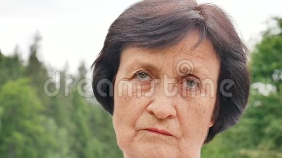 一幅有思想的悲伤的老年妇女的肖像她留着一头乌黑的短发脸上有皱纹在青山和绿林中视频的预览图