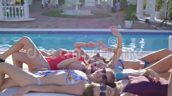 泳池派对身穿泳装身材优美的快乐女孩挥舞双手躺在泳池边近景的躺椅上视频的预览图