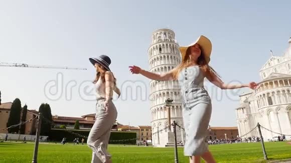 意大利比萨两个年轻快乐的女人在一个光明的日子里在比萨斜塔的背景上散步视频的预览图
